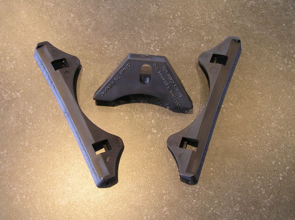 Three black plastic Optima battery hold-down brackets on a tan floor