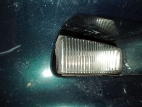 1995 Ford Taurus - Close-up of a clear ribbed front corner marker light on a dark green vehicle body.