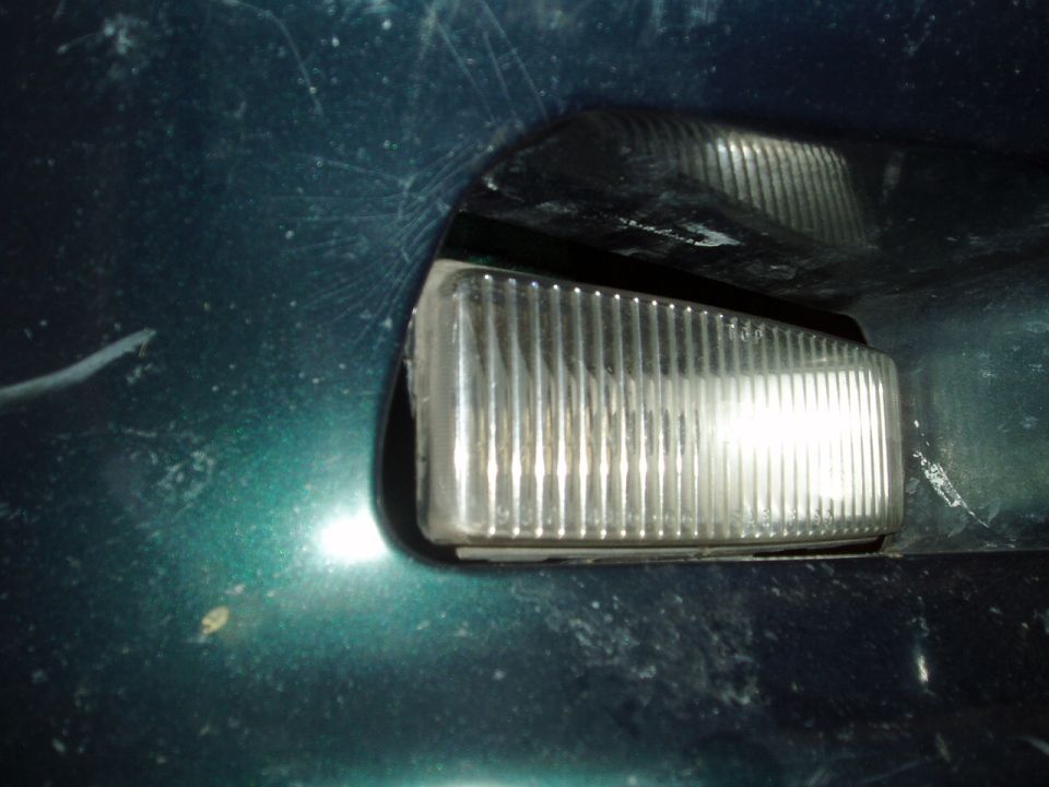 Close-up of a clear ribbed front corner marker light on a dark green vehicle body