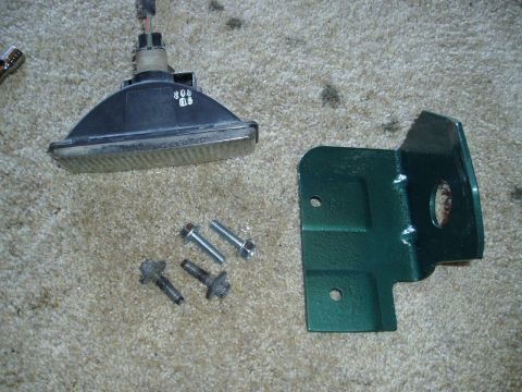 1995 Ford Taurus - A headlight assembly and mounting bracket with bolts are laid out on a carpeted surface.