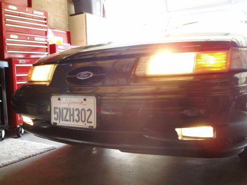 1995 Ford Taurus - The front of a 1995 Ford Taurus is shown with its lights illuminated, parked indoors.