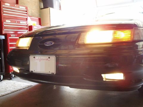 1995 Ford Taurus - Front header panel of a 1995 Ford Taurus, illuminated headlights and fog lights, with a California license plate.