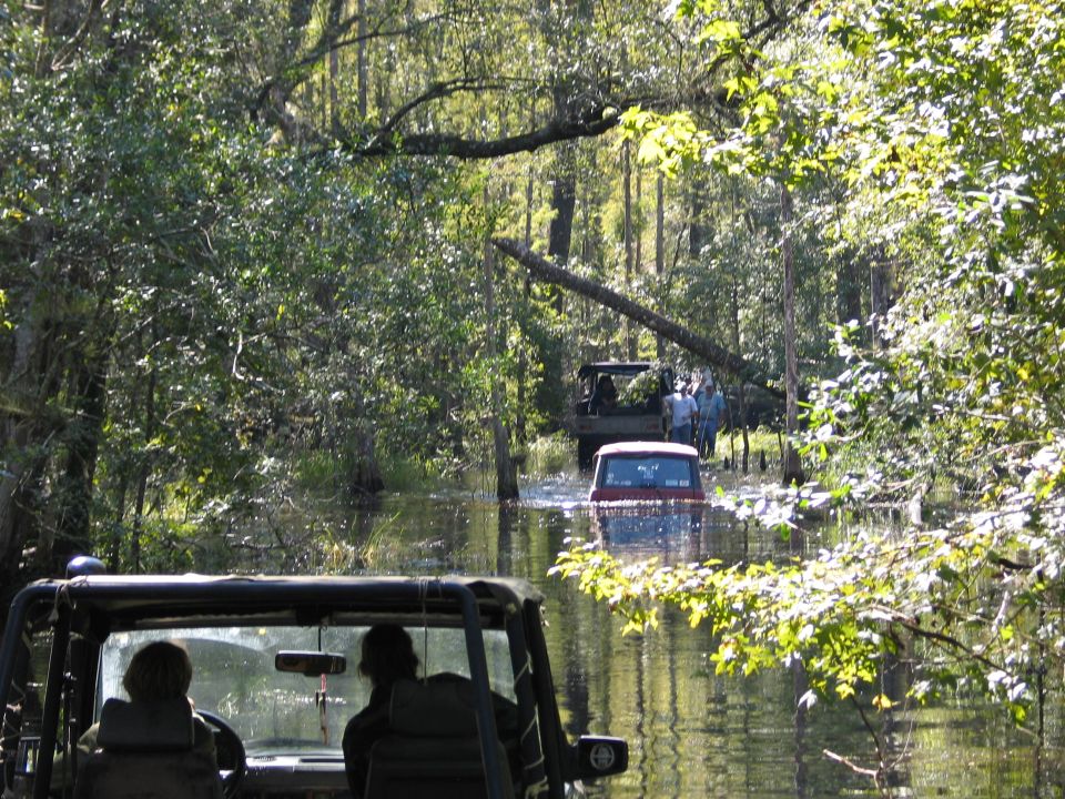 View from open vehicle of a submerged SUV and stuck rig ahead on a flooded forest trail