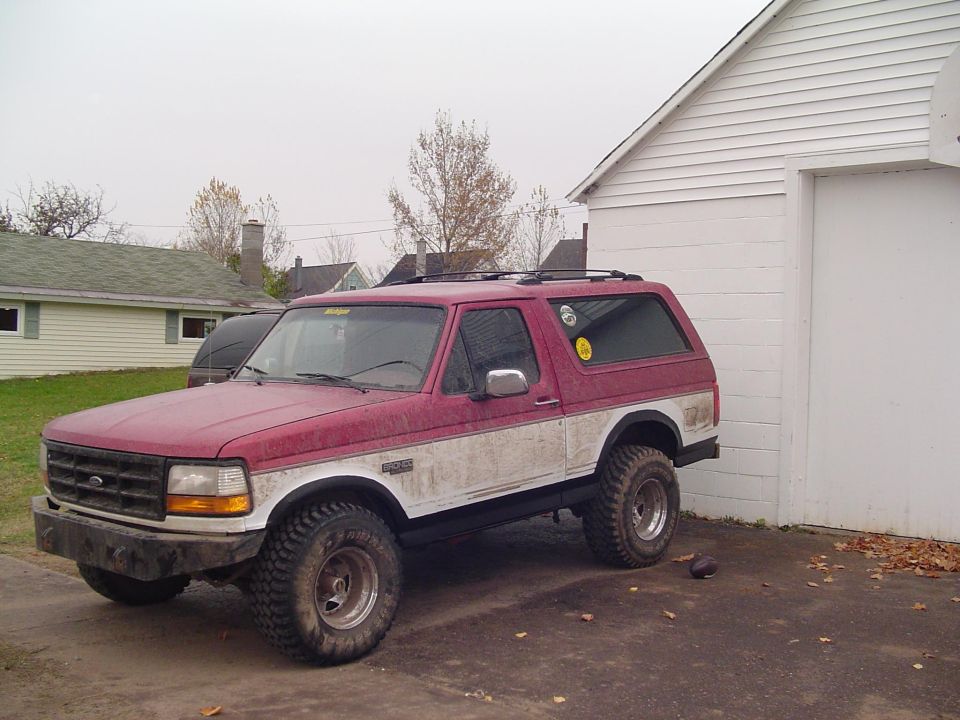 Red and white 1994 Ford Bronco parked next to a white garage