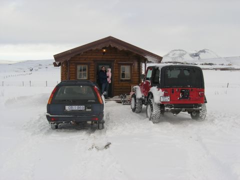 2001 Jeep Wrangler - Two vehicles are parked in the snow outside a rustic cabin, with people visible in the doorway.