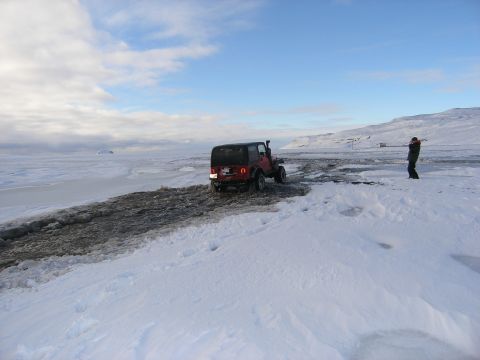 2001 Jeep Wrangler - A red Jeep TJ navigates a snowy and icy landscape, with a person observing in the background. The vehicle appears to be a 2001 model.
