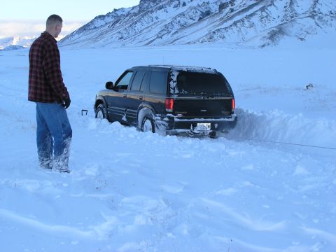 2001 Jeep Wrangler - SUV is stuck in the snow, a man is standing nearby and a tow rope is attached.
