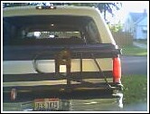 1993 Ford Bronco - Very small, low-resolution photo of the rear of a two-tone light-and-dark full-size SUV parked on grass, showing the tailgate, rear window,…