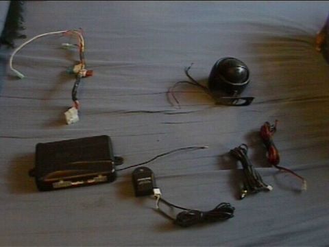 1994 Ford Probe - Various car alarm components are spread out on a grey surface, including a control module and a siren.