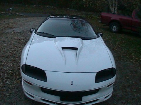 1996 Chevrolet Camaro - A white 1996 Chevrolet Camaro is parked outside with a red pickup truck in the background.
