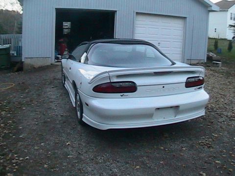 1996 Chevrolet Camaro - The rear of a white 1996 Chevrolet Camaro is visible, parked on a gravel driveway in front of an open garage.