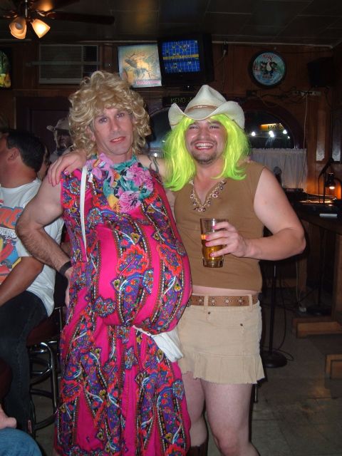 1989 Ford Bronco - Two men dressed in drag pose for a photo while holding drinks at a dimly lit bar.