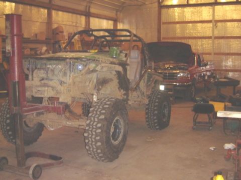 1992 Ford Bronco - A heavily modified off-road vehicle sits in a garage, with a red pickup truck visible in the background.