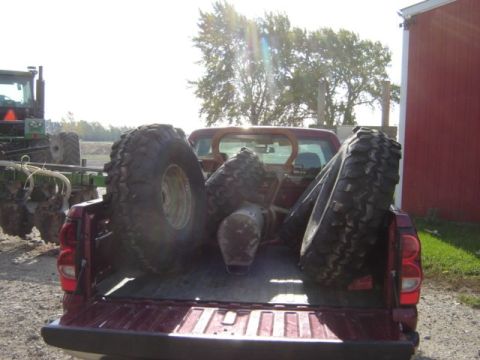 1992 Ford Bronco - A red pickup truck bed is filled with large off-road tires, with a tractor visible in the background.