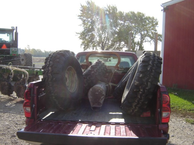 Red pickup truck bed with large tires; tractor in background