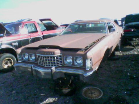 1979 Ford F-150 - A brown sedan, possibly a 1977 model, sits in a junkyard with its hood open and front end visible.