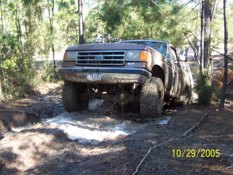 1987 Ford Bronco - A brown 1987 Ford F-Series truck navigates a muddy trail in a wooded area.