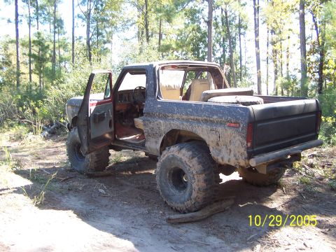 1987 Ford Bronco - This muddy SUV is parked off-road with its doors open, showing its interior and large tires.