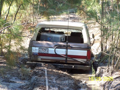 1987 Ford Bronco - This 1987 Ford Bronco is stuck in a muddy trail, with a cooler visible in the cargo area.