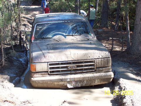 1987 Ford Bronco - A muddy 1987 Ford Bronco navigates a difficult off-road trail, getting stuck in a deep mud pit.