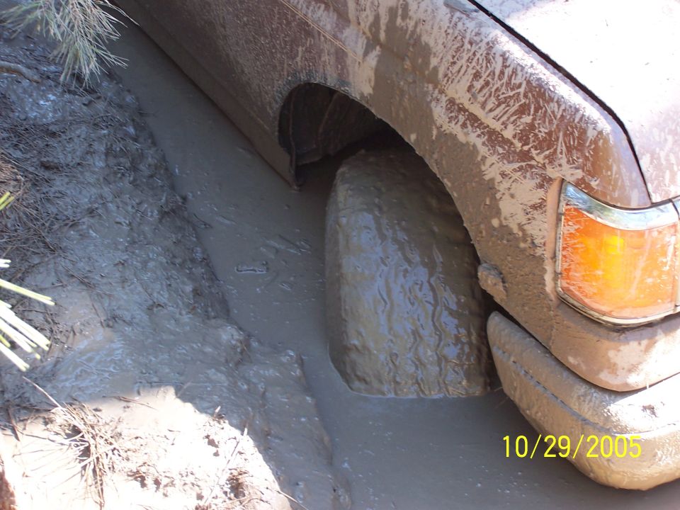 Muddy side view of a vehicle with its front wheel deep in mud