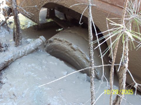 1987 Ford Bronco - A vehicle is deeply stuck in thick mud, with only a portion of its tire and undercarriage visible.