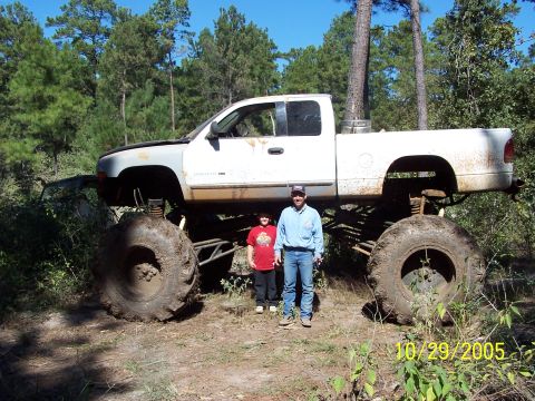 1987 Ford Bronco - A heavily modified pickup truck with oversized tires sits in a wooded area.