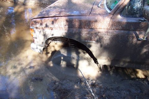1987 Ford Bronco - A brown SUV is stuck in thick mud, with only the front driver's side visible.