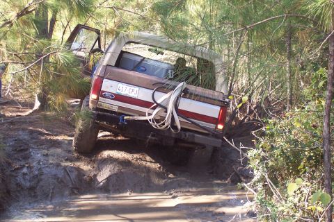 1987 Ford Bronco - Ford Bronco navigating a muddy trail with trees and brush surrounding it.
