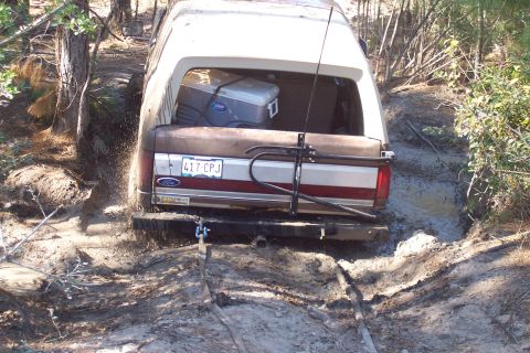 1987 Ford Bronco - A Ford Bronco is stuck in a muddy trail, with a cooler visible in the back.