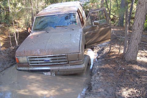 1987 Ford Bronco - A 1987 Ford Bronco is stuck in a muddy ditch, its front end submerged in water and mud.