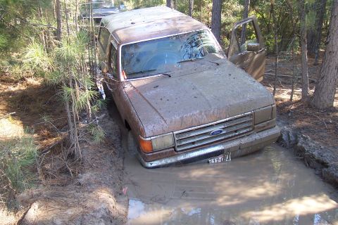 1987 Ford Bronco - This 1987 Ford Bronco is stuck in a muddy ditch, with another vehicle partially visible behind it.
