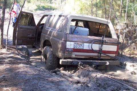 1987 Ford Bronco - This 1987 Ford Bronco is stuck in the mud on a wooded trail, with its doors open and people nearby.