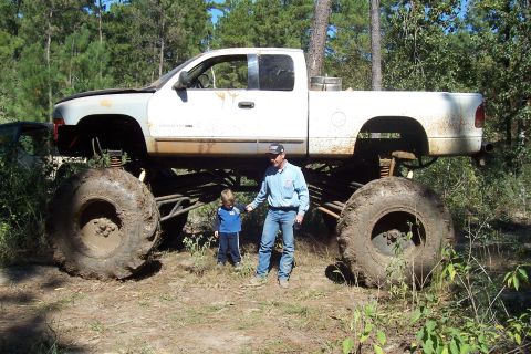 1987 Ford Bronco - Monster truck with two people standing beside it in a wooded area.