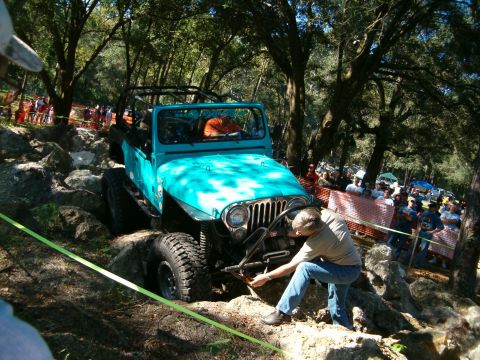 1991 Ford Bronco - A teal Jeep Wrangler tackles a challenging off-road course, with a person attending to the front winch.
