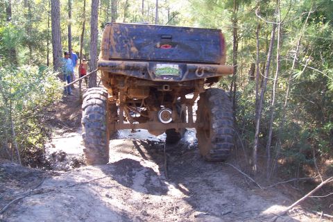 1987 Ford Bronco - A heavily modified pickup truck navigates a muddy off-road trail.