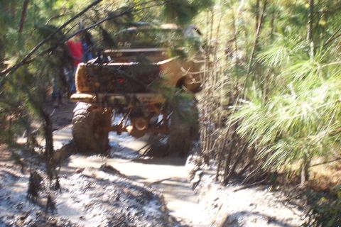 1987 Ford Bronco - Off-road vehicle navigating a muddy path in a forest environment.