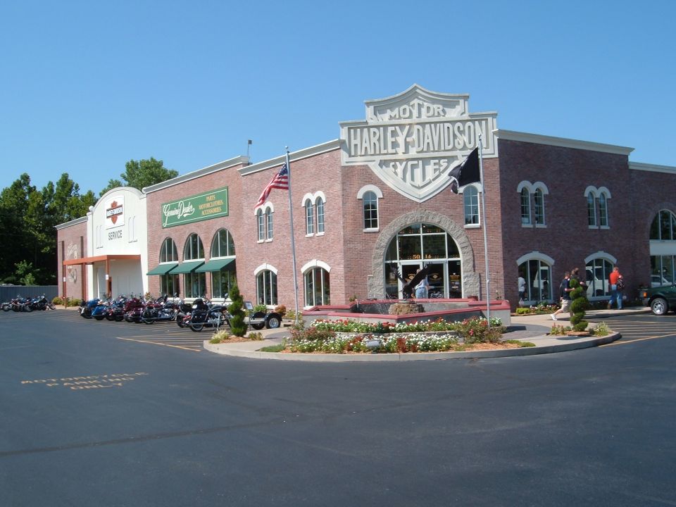 Harley-Davidson dealership building exterior with motorcycles parked in front and a green car on the right