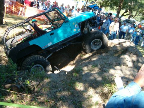 1991 Ford Bronco - Modified Jeep Wrangler tackling an off-road course with spectators observing. The vehicle appears to be from the early 1990s.