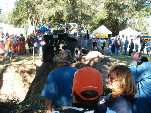1991 Ford Bronco - A modified Jeep navigates an obstacle course with onlookers gathered around.