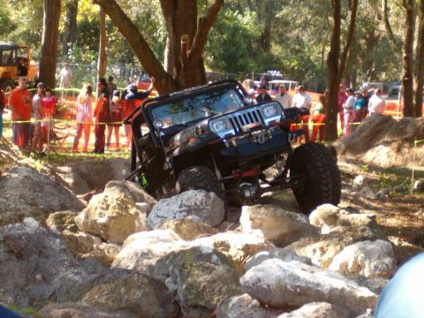 1991 Ford Bronco - Off-road Jeep Wrangler TJ tackling a rocky obstacle course with a crowd observing.
