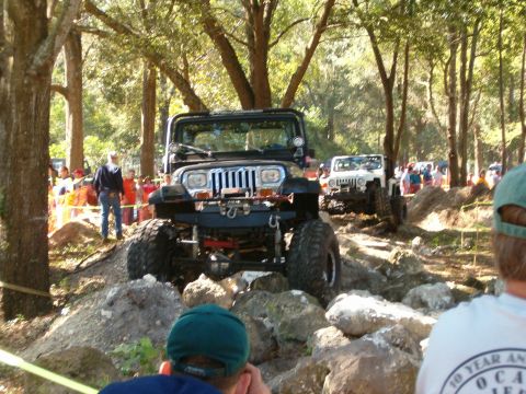 1991 Ford Bronco - Two Jeeps tackle a challenging off-road course with spectators observing the action.