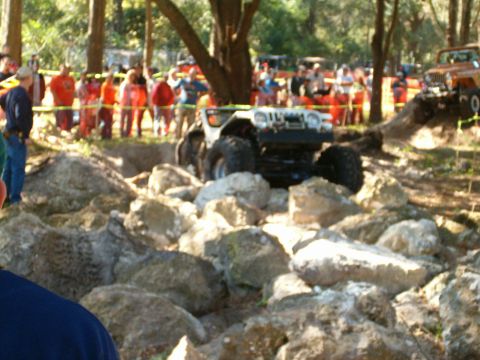 1991 Ford Bronco - An off-road vehicle tackles a rocky obstacle course with a crowd gathered to observe the event.
