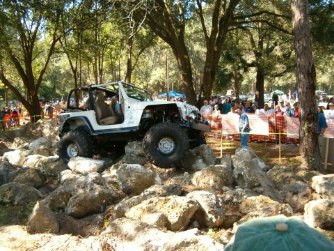 1991 Ford Bronco - A modified Jeep Wrangler navigates a challenging rock obstacle during an off-road event.