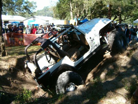 1991 Ford Bronco - A white Jeep Wrangler TJ is stuck in a ditch during an off-road event, with spectators watching.