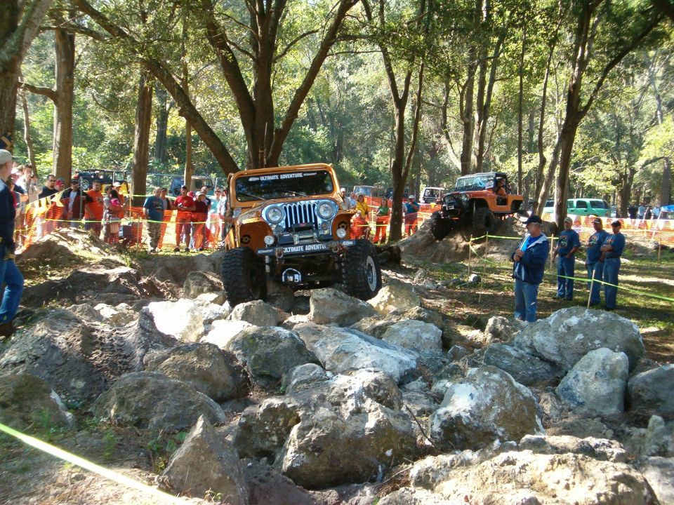 Orange Jeep Wrangler navigating a rocky obstacle course with spectators watching