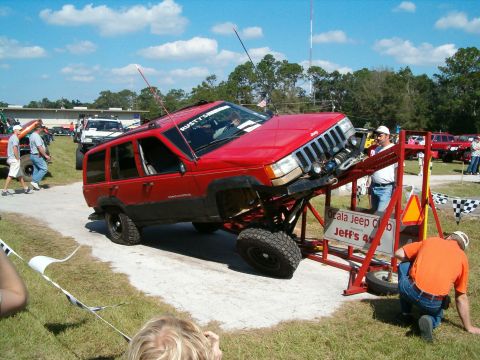 1991 Ford Bronco - A modified Jeep Grand Cherokee is positioned on an obstacle course at an outdoor event with spectators present.