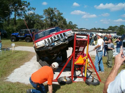 1991 Ford Bronco - A red Jeep Grand Cherokee is positioned on a tilting platform during an event with spectators.
