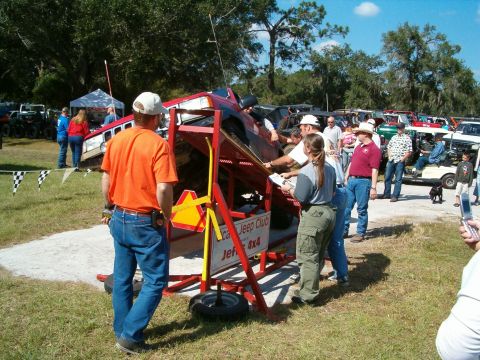 1991 Ford Bronco - A red Jeep is positioned on a tilting apparatus at an outdoor event, with several people observing.