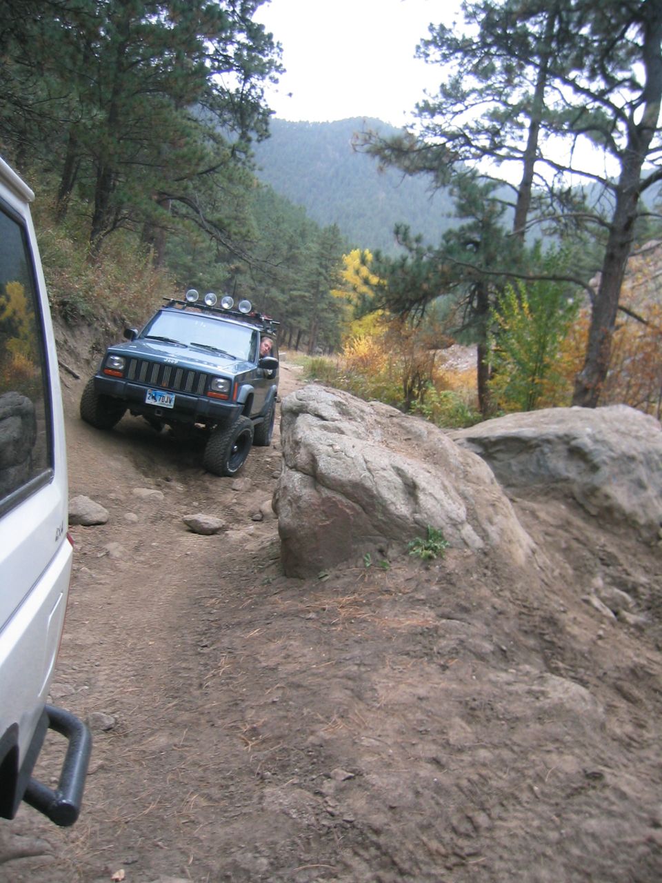 Blue 1997 Jeep Cherokee on a rocky trail, with a white vehicle in the foreground